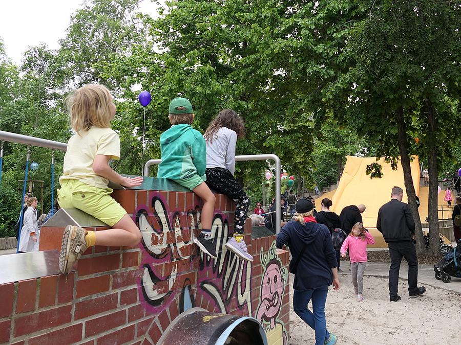 Drei Kinder rittlings auf Klinkermauer auf Spielplatz im Grünen