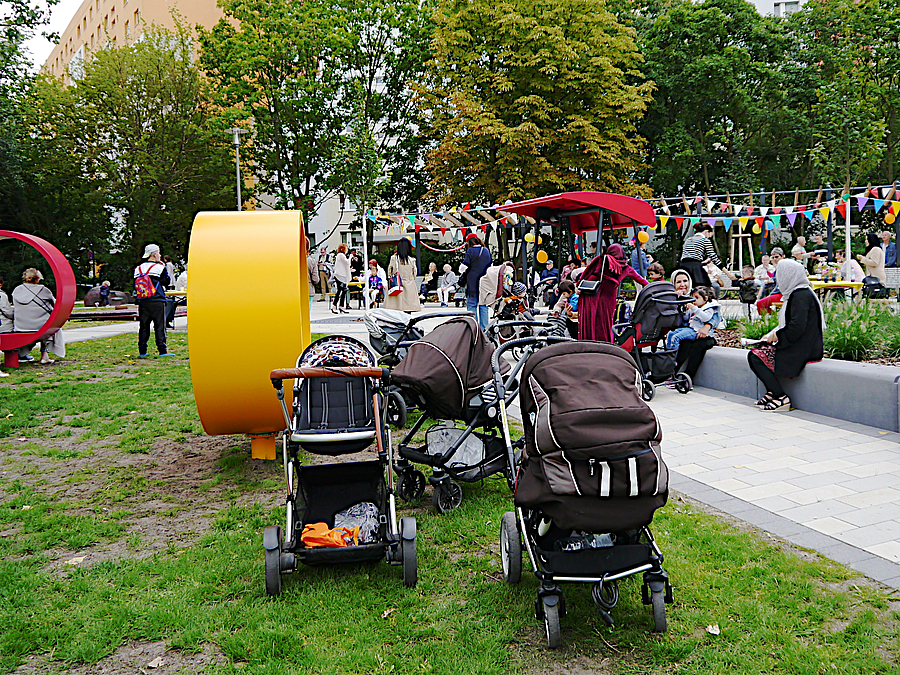 Kinderwagen vor gelbem Ring auf Rasen, viele Menschen im Grünen