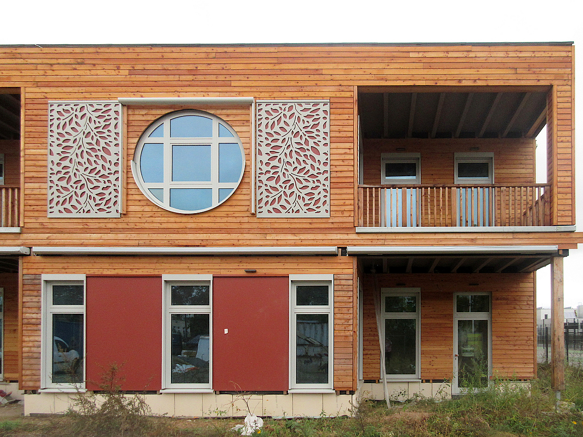 Fassade zweistöckiger Holzbau mit teils runden Fenstern, Loggia und Schmuckornamenten in Blätterform