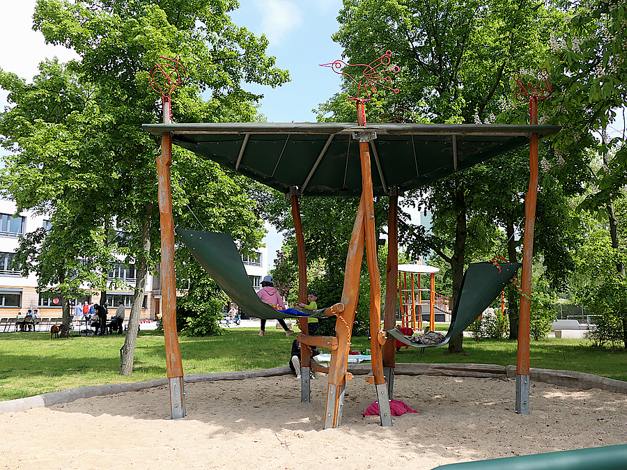 2 Kinder auf Hängematten in überdachtem Pavillon aus Holz auf Sandfläche