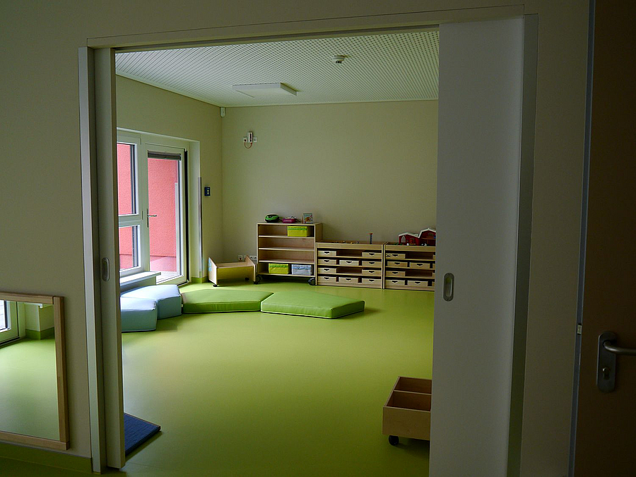 Raum mit Schiebetür, grüner Boden, kleine Möbel