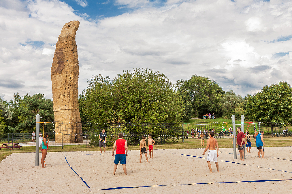 Spiel auf Beachvolleyballfeld vor Felsnadel und Grün