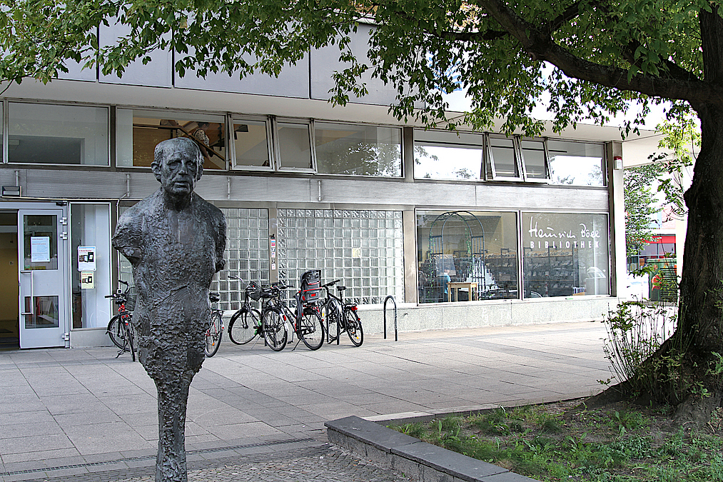 Plastik des Autors vor Eingang mit Schaufenstern