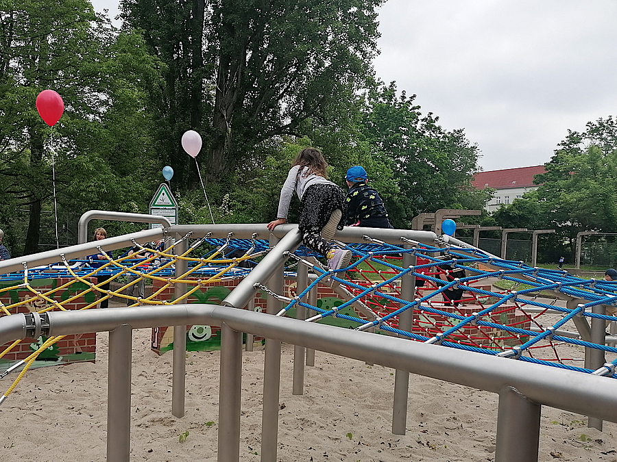 Zwei Kinder klettern über horizontales Netz auf Stahlstützen und Klinkermauern im Grünen