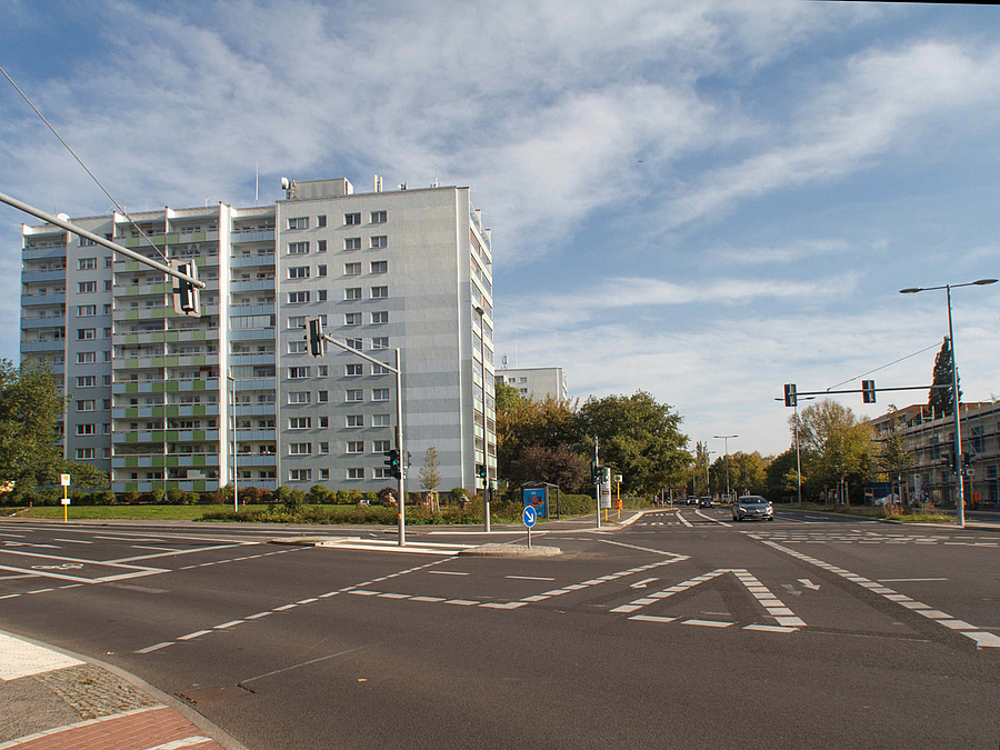 Sehr breite Straßenkreuzung mit Fahrradmarkierungen, Plattenbauten