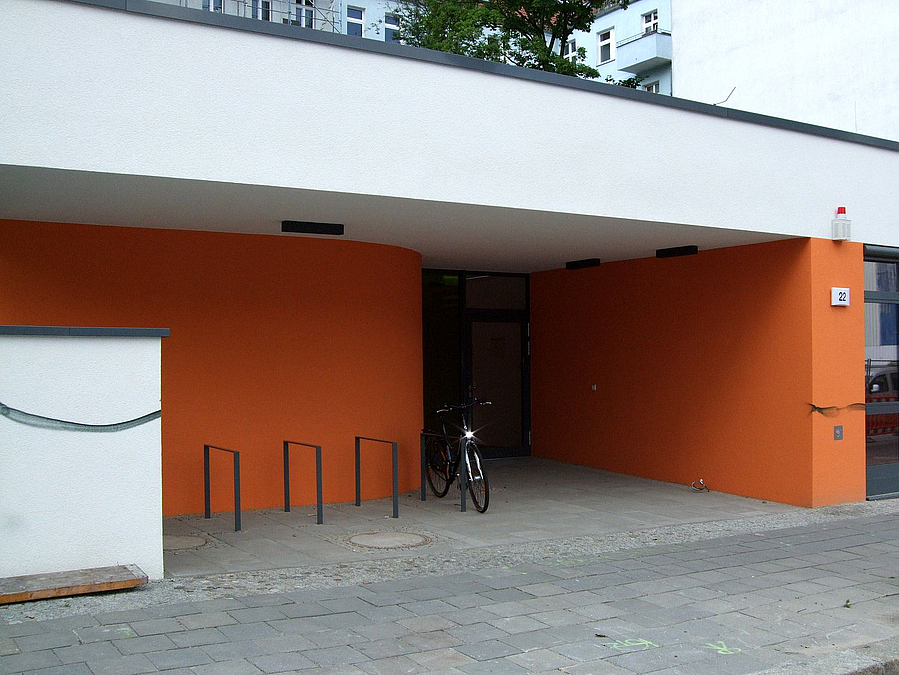 Flachbau in Orange und Weiß, eine gerundete Wand am Eingang