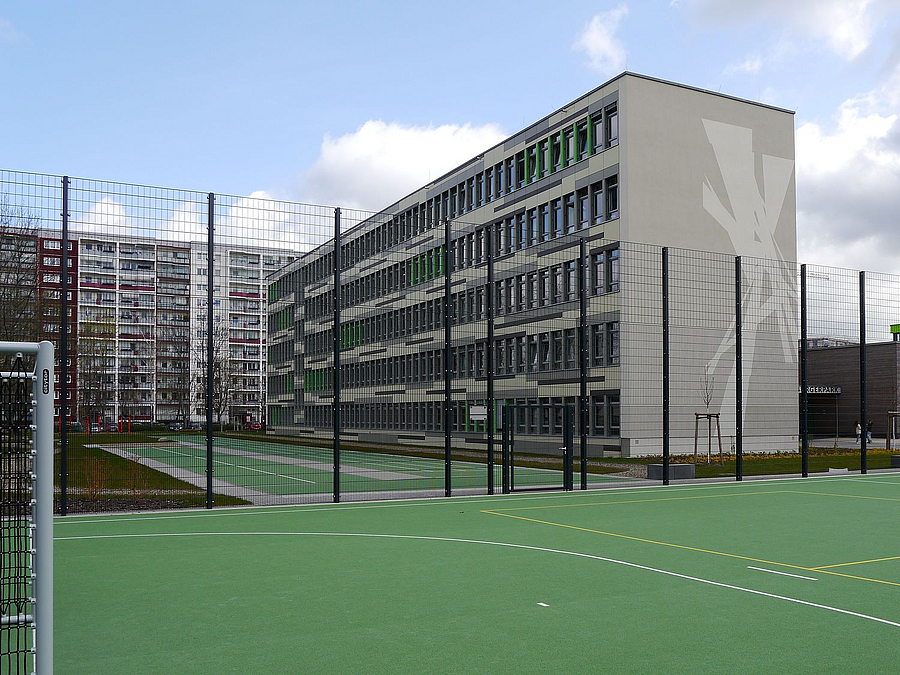 Sportplatz, hoher Zaun, Schulgebäude