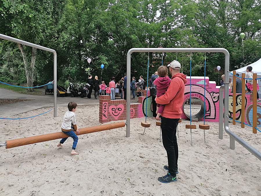 Mann mit Kindern auf Spielplatz im Grünen, bunt bemalte Klinkermauern