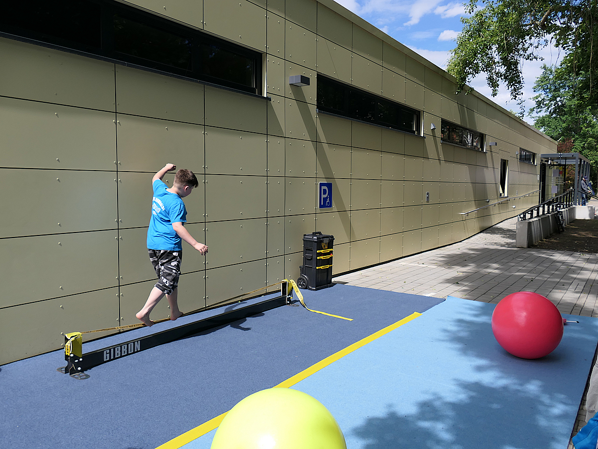 Ein Junge balanciert außen an der Sporthalle, daneben bunte Pezzi-Bälle