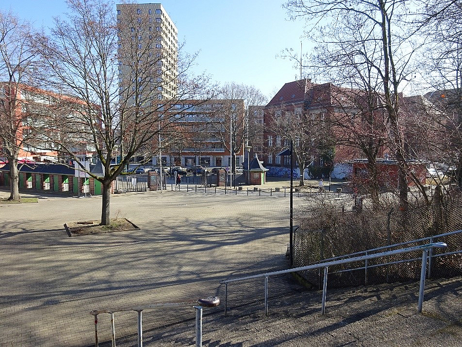Platz mit Baum im Winter, im Hintergrund Kassenhäuschen, städtisches Umfeld