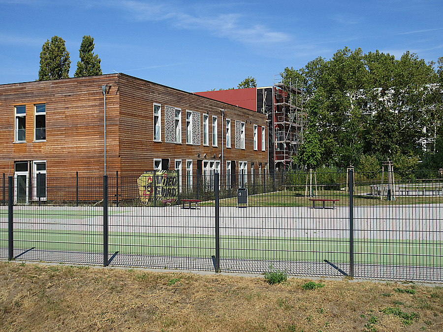 Zweistöckiger Holzbau hinter Zaun und grüner Laufbahn