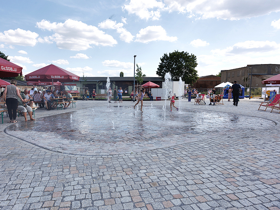 Platz mit Natursteinpflaster und Kindern im Fontänenfeld