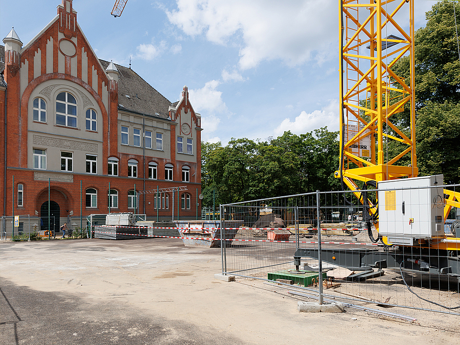 Kran und Baumaterial vor altem Schulgebäude