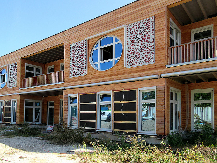 Fassade zweistöckiger Holzbau mit teils runden Fenstern, Loggia und Schmuckornamenten in Blätterform