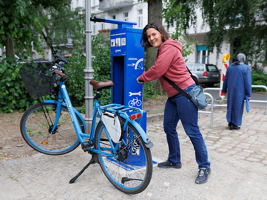 Frau mit Fahrrad an blauer Säule mit Werkzeugen
